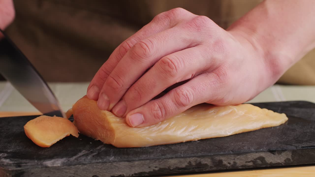 Cutting with knife raw chicken meat on desk close-up. Preparing raw food for cooking. Grilled chicken, duck, turkey kebab with vegetables.