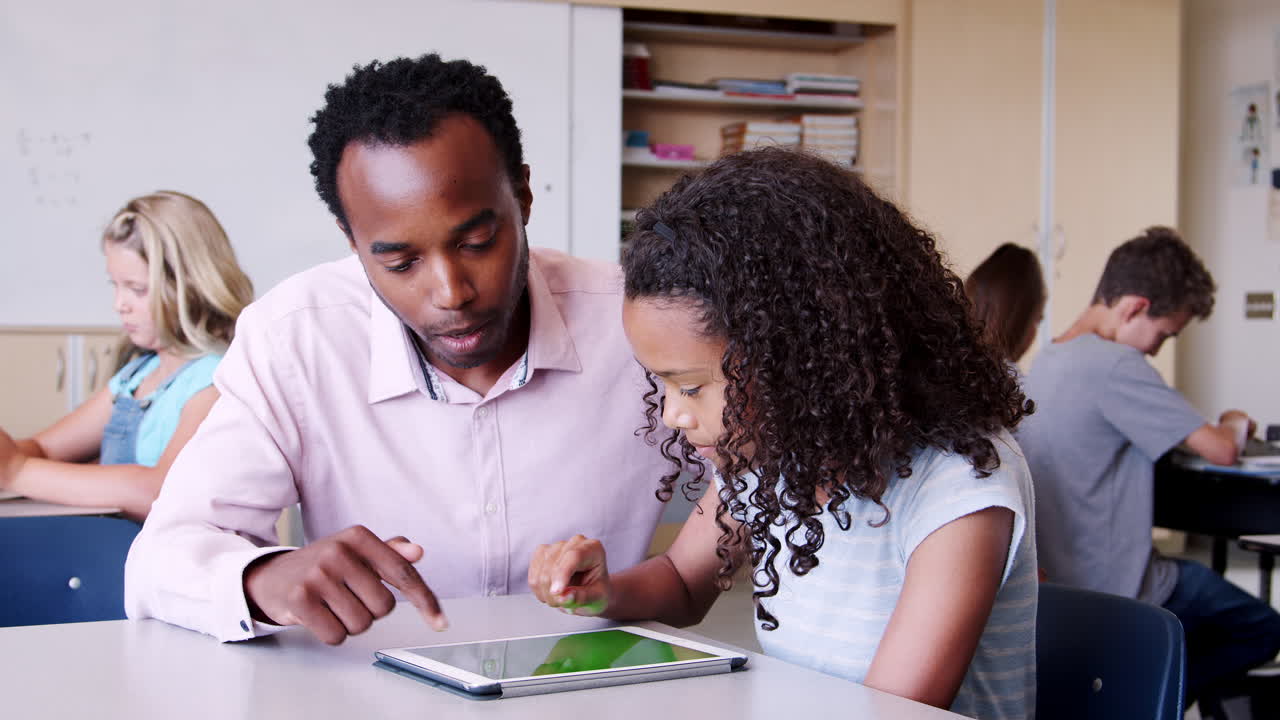 Elementary school teacher helping schoolgirl with tablet