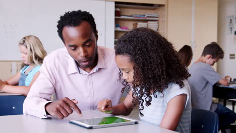 elementary school teacher helping schoolgirl with tablet