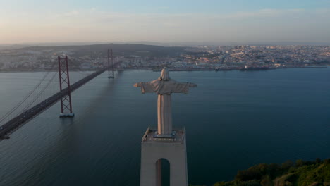 Zurück-Luftaufnahme-Des-Heiligtums-Von-Christus-Der-König-Statue-Mit-Der-Roten-Brücke-Ponte-25-De-Abril-In-Lissabon,-Portugal