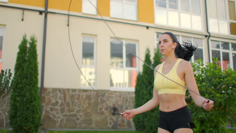 a young beautiful girl jumps on a skipping rope in a park in slow motion in sports clothes. play sports against the background of houses