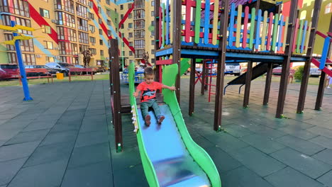 caucasian toddler in bright t-shirt and pants playing on the playground. kid slides to the ground and runs away.