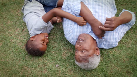 El-Abuelo-Y-El-Nieto-Negros-Juegan-Tumbados-En-El-Césped,-Vista-Aérea