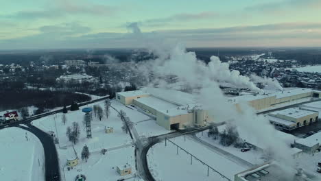 aerial view flying in front of a large smoking plant on o cold winter evening