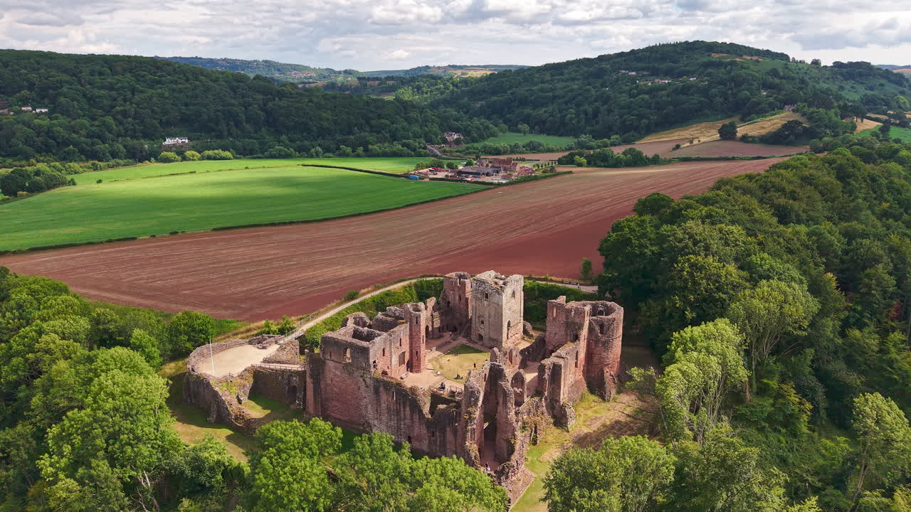 Flying over historic castle ruins surrounded by lush forests and farmed fields