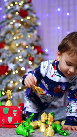 beautiful toddler boy sits on the floor playing with gift boxes and candies. happy christmas time for kids. vertical video
