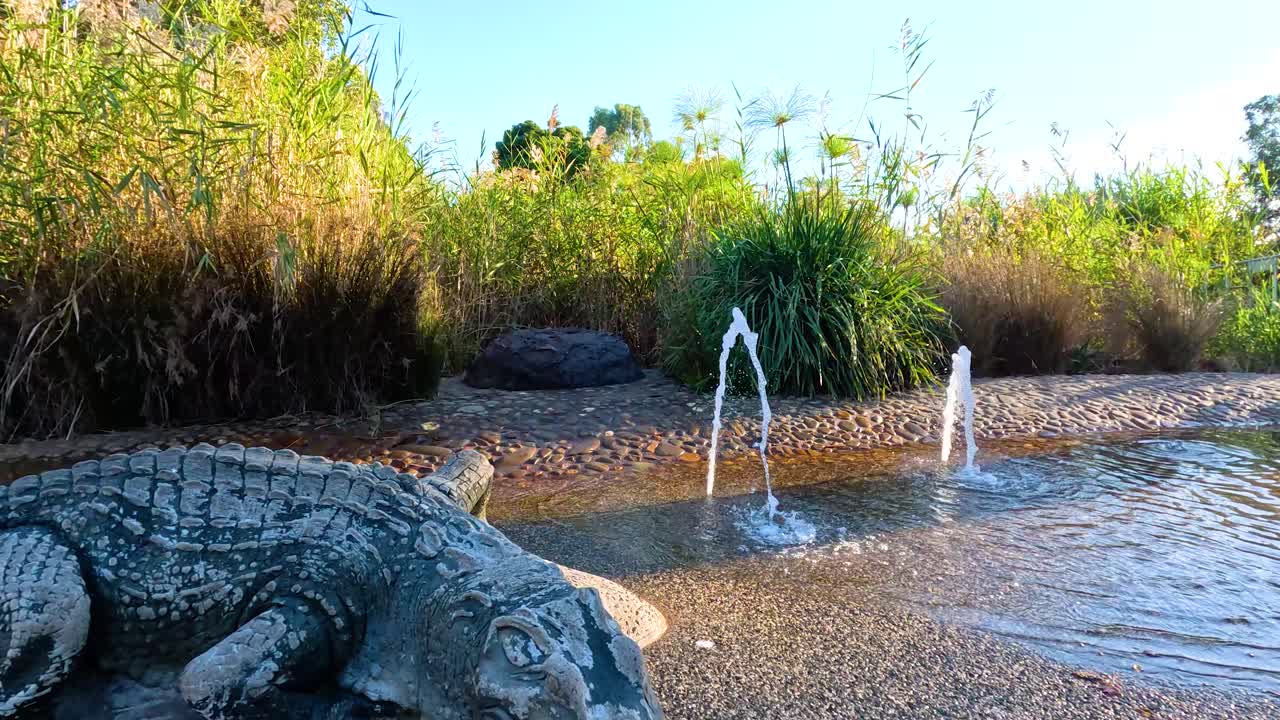 fuentes de agua y escultura de cocodrilo en un exuberante entorno de zoológico