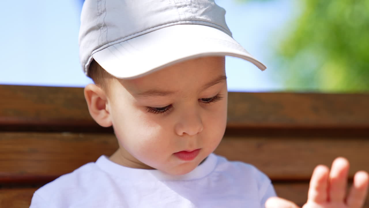 Cropped image of a little Caucasian kid wearing a cap. Cute baby boy looking down and waving hand. Close up.