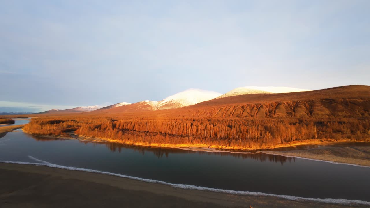 Witness the stunning natural beauty of Yakutia as the sun sets, illuminating the vast terrain. The serene river winds through the majestic mountains, revealing nature's tranquil charm.