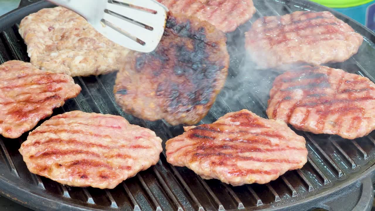 Slow motion close up of a vendor flipping beef patties on a smoky outdoor grill