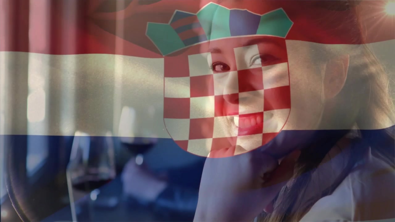 Siedząca kobieta odwraca się, gdy kamera panoramuje, uśmiechając się do przyjaciółki, z kieliszkiem wina, a nakładka z flagą animuje jedzenie.