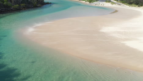 Tilting-up-drone-shot-of-the-wind-blowing-sand-across-a-sand-bar-at-Hat-Head-New-South-Wales,-Australia