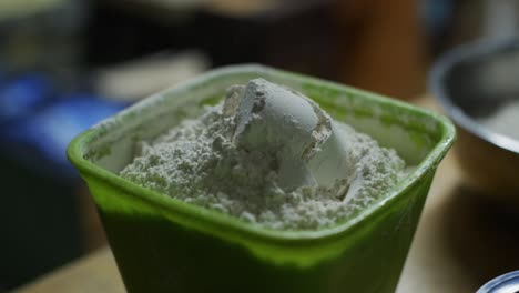 plastic cup full of plain white flour tipped into green plastic container, filmed as closeup slow motion shot