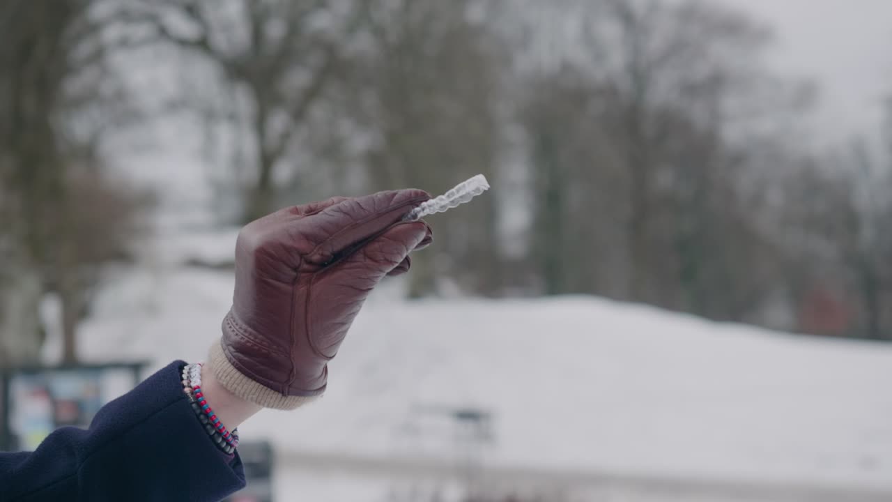 Hand with leatrher glove showing an invisible aligner, winter day, close up shallow depth of field
