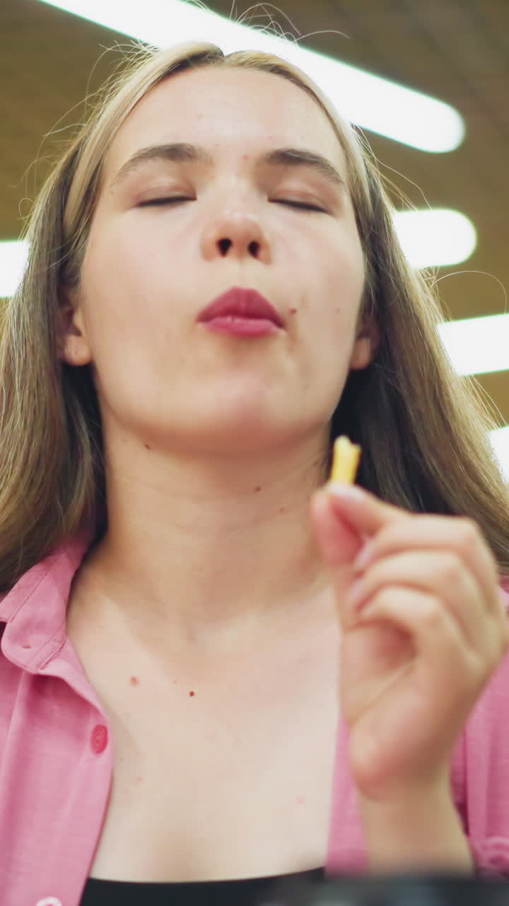 레스토랑에 앉아있는 여성은 감자김을 한 어 먹고, 만족으로 눈을 감고 머리를 흔들며, 맛있는 음식을 즐기고, 흐릿한 배경과 함께 밝은 레스토랑 조명을 즐기고 있습니다.