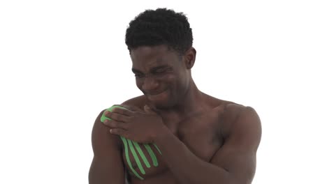 vista frontal de un atleta masculino afroamericano haciendo movimientos circulares del hombro superando el dolor. tratamiento de hombro lesionado por cinta de kinesiología. aislado en fondo blanco
