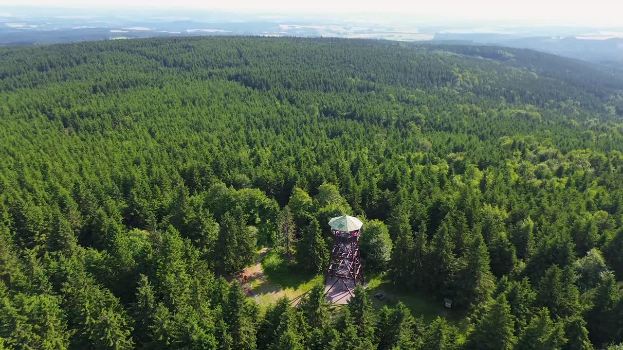 Drone view as it flies over the trees and rotates away from the lookout tower on the mountains with the valley in the background