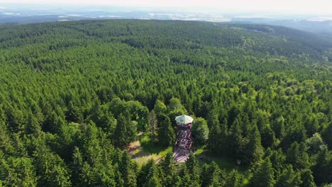 Drone-view-as-it-flies-over-the-trees-and-rotates-away-from-the-lookout-tower-on-the-mountains-with-the-valley-in-the-background