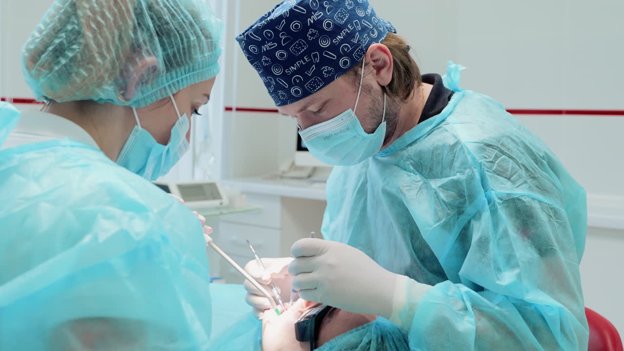 VINNYTSIA, UKRAINE - MAY 20, 2023: Dentists in green coats treat the teeth of a patient sitting in a chair. Modern dental clinic. Healthcare oral aesthetic treatment