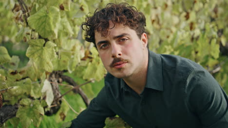 happy young winegrower looking camera at grape plantation vertically closeup