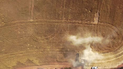 straight down aerial view of a combine harvesting crops and spreading dust up into the sky