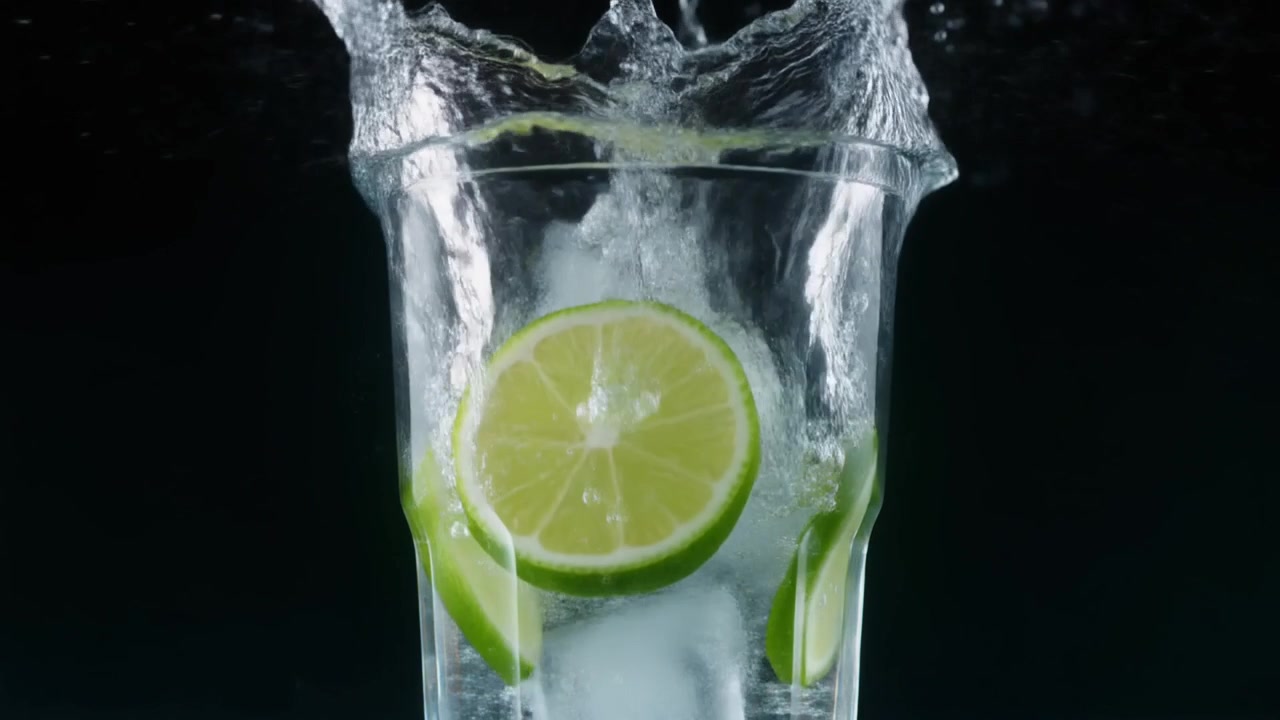 Fetta di lime che cade in un bicchiere di acqua frizzante