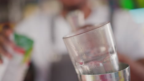 el camarero vierte jugo en una taza de vidrio en un bar de primer plano. el camarero negro agrega ingrediente para un delicioso cóctel en el club. el barman prepara una bebida para los invitados