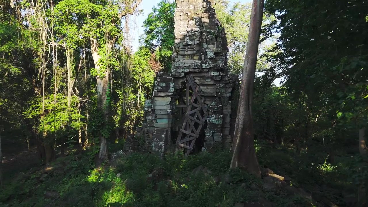 Tayland sınırı yakınlarındaki uzak bir orman kompleksinde gizlenmiş tapınak yapısı üzerindeki dev kumtaşı yüzler. Drone ile gür orman üzerinde havadan geçiş.