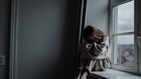 una chica triste sentada junto a la ventana.