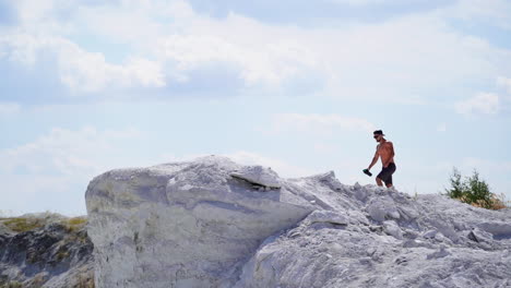 slow motion of strong athlete in the mountains. shirtless sportsman walking up the white hill in summer. muscular man exercises outdoors.