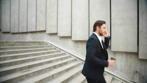 business man running on stairs in city. male employee talking on smartphone