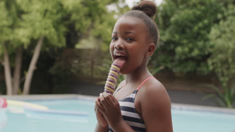 una chica afroamericana feliz sonriendo y comiendo helado junto a la piscina, en cámara lenta, sin alteración.