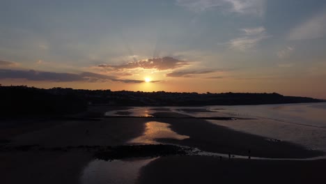 Sunset-rays-beam-fiery-golden-colours-across-relaxing-beach-ocean-coastline-aerial-view-slow-descend