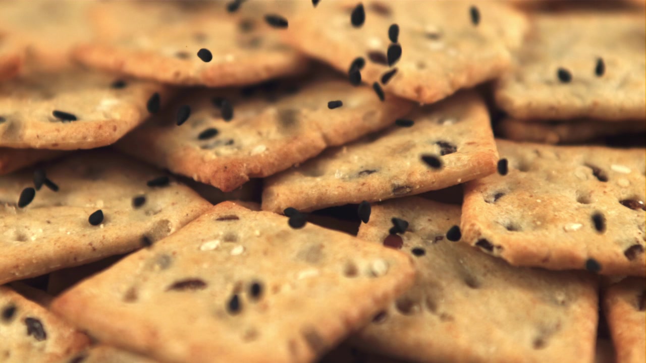Graines noires tombant sur des crackers salés au ralenti