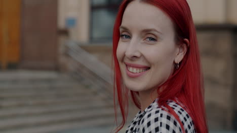woman with red hair smiling in front of a building