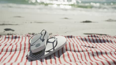 Close-up-of-flip-flops-and-towel-on-beach,-in-slow-motion,-with-copy-space