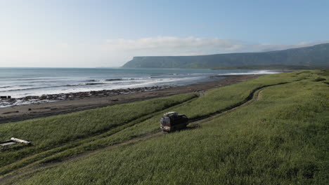 Drone-view-Watch-out-for-a-black-car-driving-along-a-dusty-road-along-the-ocean