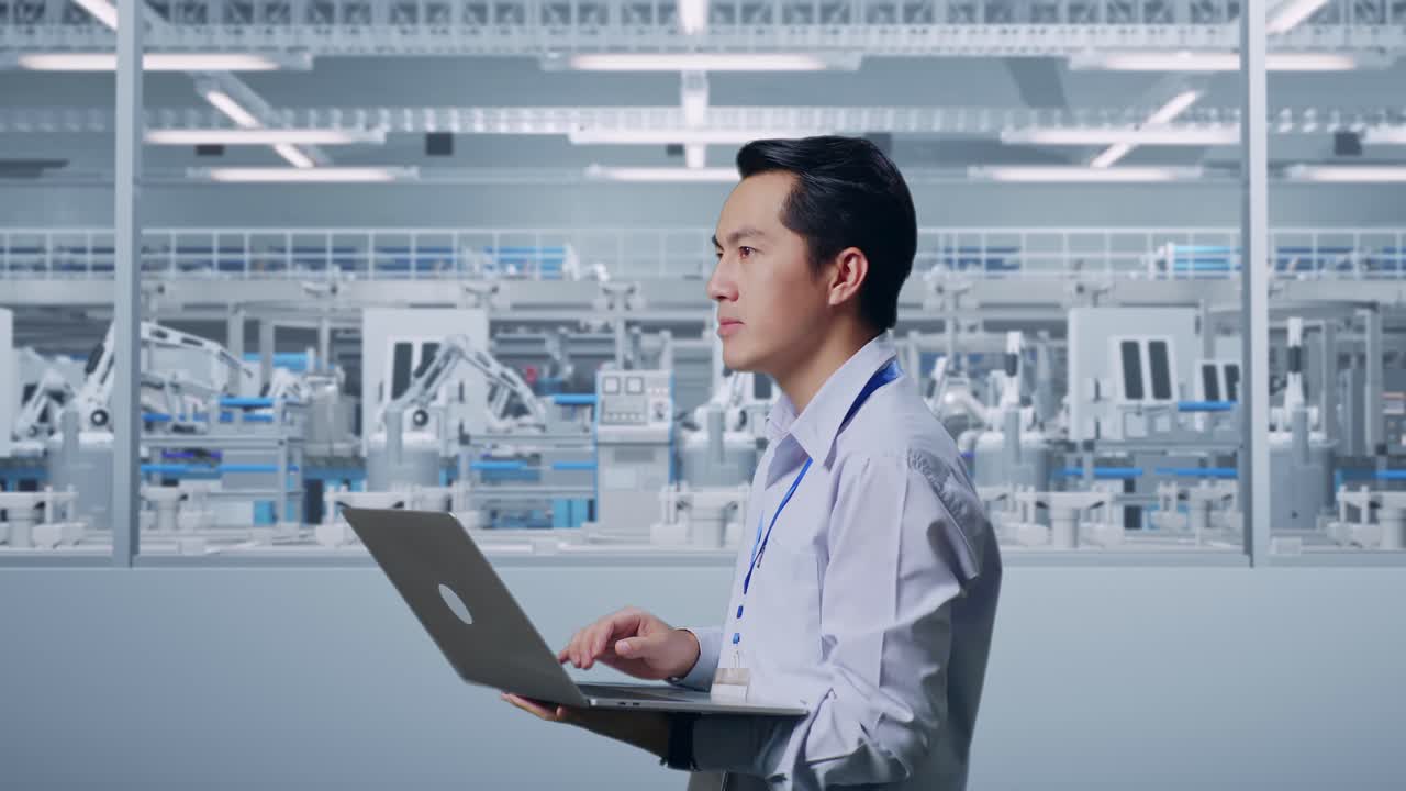 Side View Of An Asian Male Professional Worker Standing At Factory Digitalization, Observes By Looking Up Before He Come To Concentrating On The Laptop And Keep On Typing
