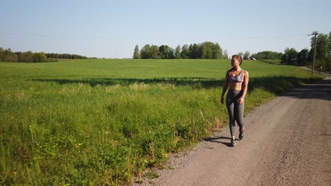 eine junge, fitte frau in leggings und einem sport-bh-oberteil joggt an einem sonnigen sommertag alleine in der schwedischen landschaft