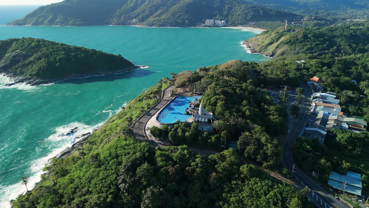 Aerial tilt-up push-back reveal over Promthep Cape’s blue plaza to rocky headland, Phuket