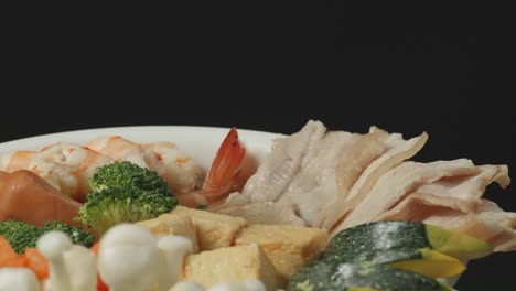 close up of a bowl of sukiyaki or shabu spinning around on the black background