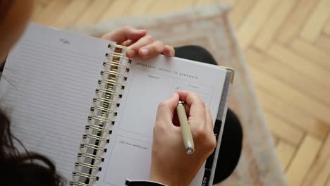 Woman-writing-down-important-things-to-do-in-her-schedule-planner,-over-the-shoulder-shot