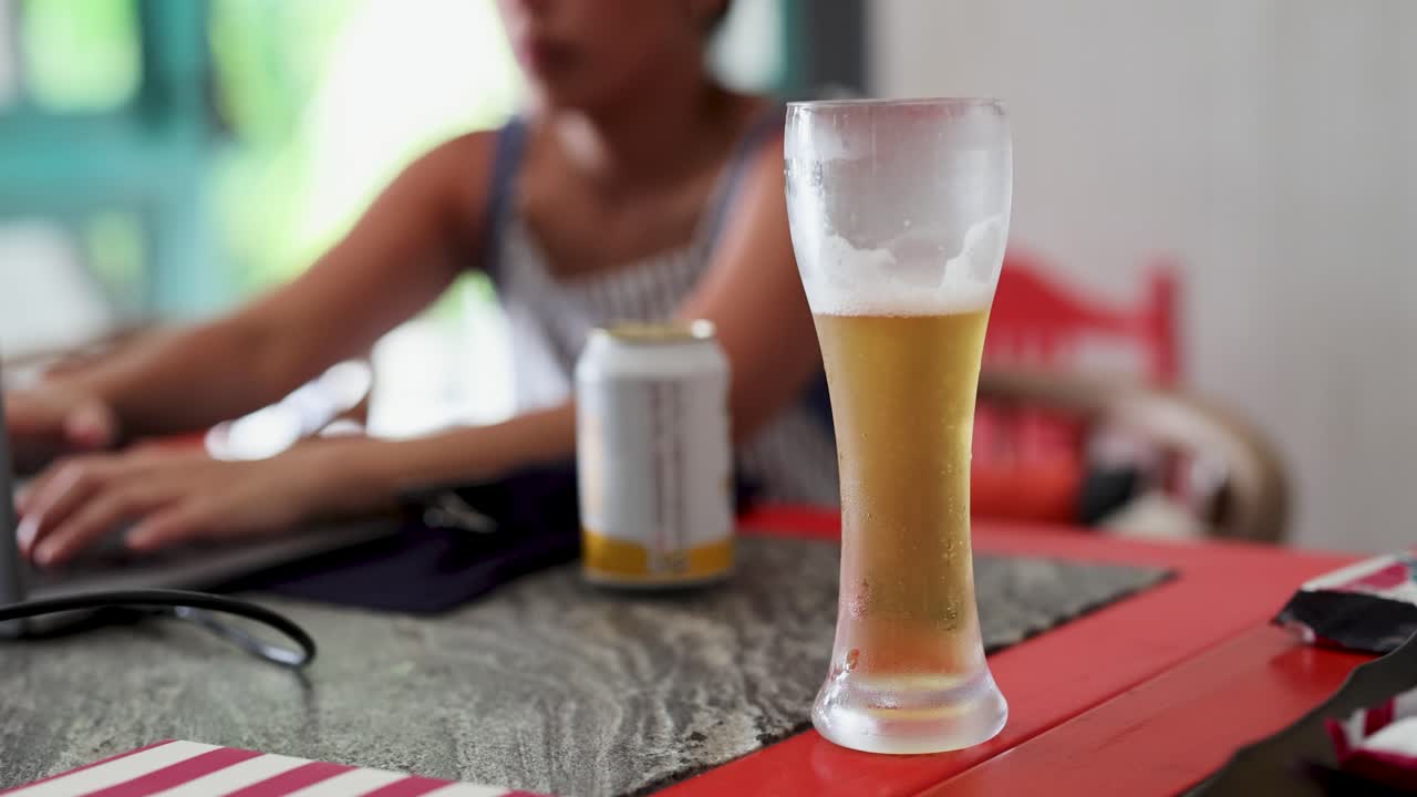 una persona escribe en una computadora portátil en una cafetería, con una cerveza en foco. atmósfera brillante y casual