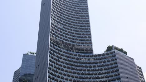 upward camera tilt reveals modern singapore high-rise with geometric facade, urban greenery, and bright daylight