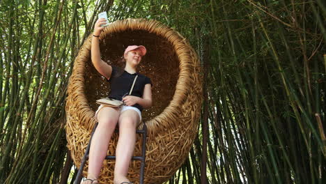 young girl taking selfie in wicker egg shaped seat in oriental bamboo forest