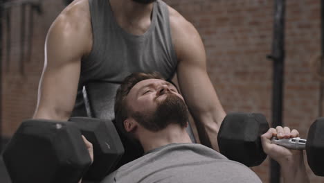 coach controlling man lifting big dumbbells