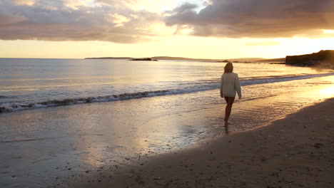 woman strolling along the water at sunset