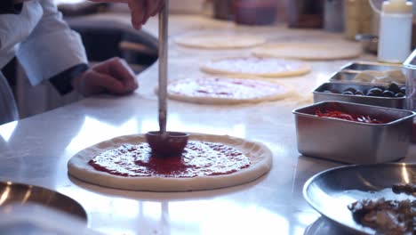 Chef-adds-tomato-sauce-on-top-of-pizza-Neapolitana-on-the-kitchen-table