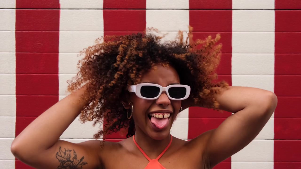 Happy Young Woman with Curly Hair and Sunglasses Against a Striped Wall