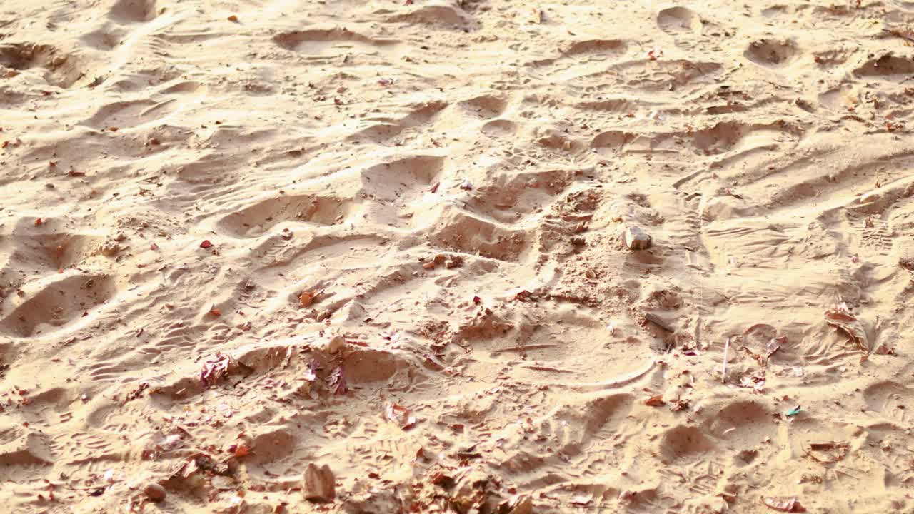 A sandy beach in Phuket, Thailand, with visible footprints and textured patterns under bright sunlight